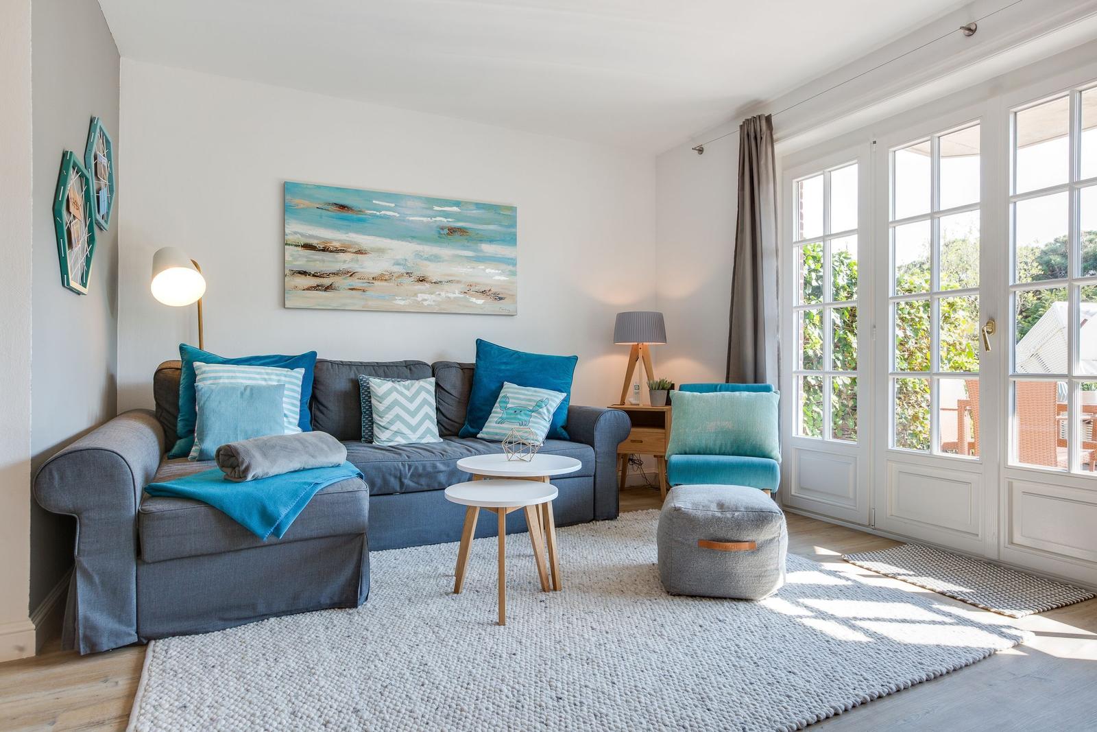 Wohnzimmer mit Sofa, Sitzhocker und französischen Fenstern.