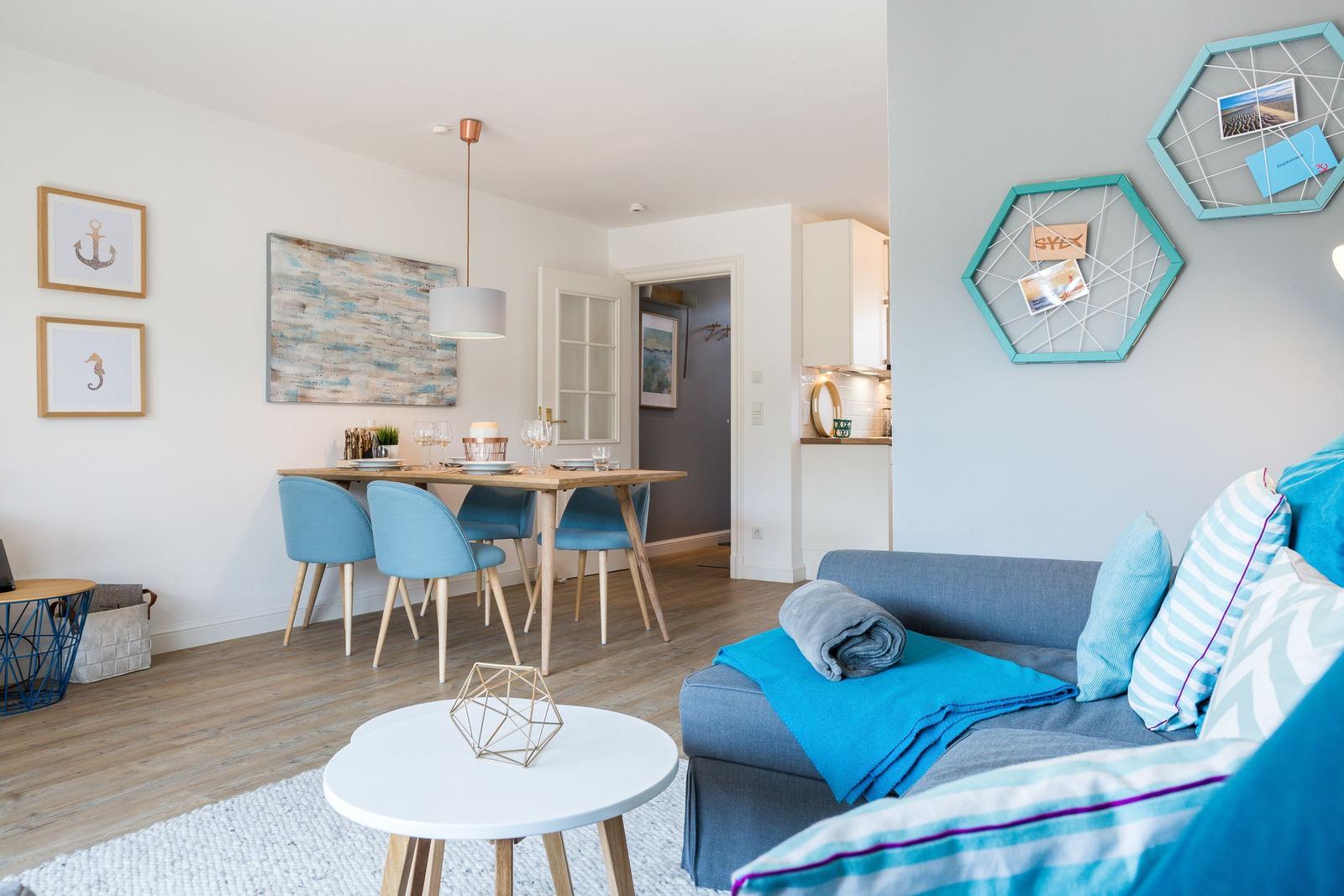 Wohn- und Essbereich mit blauen Stühlen und Sofa. Wanddekoration mit Seehund und Anker.