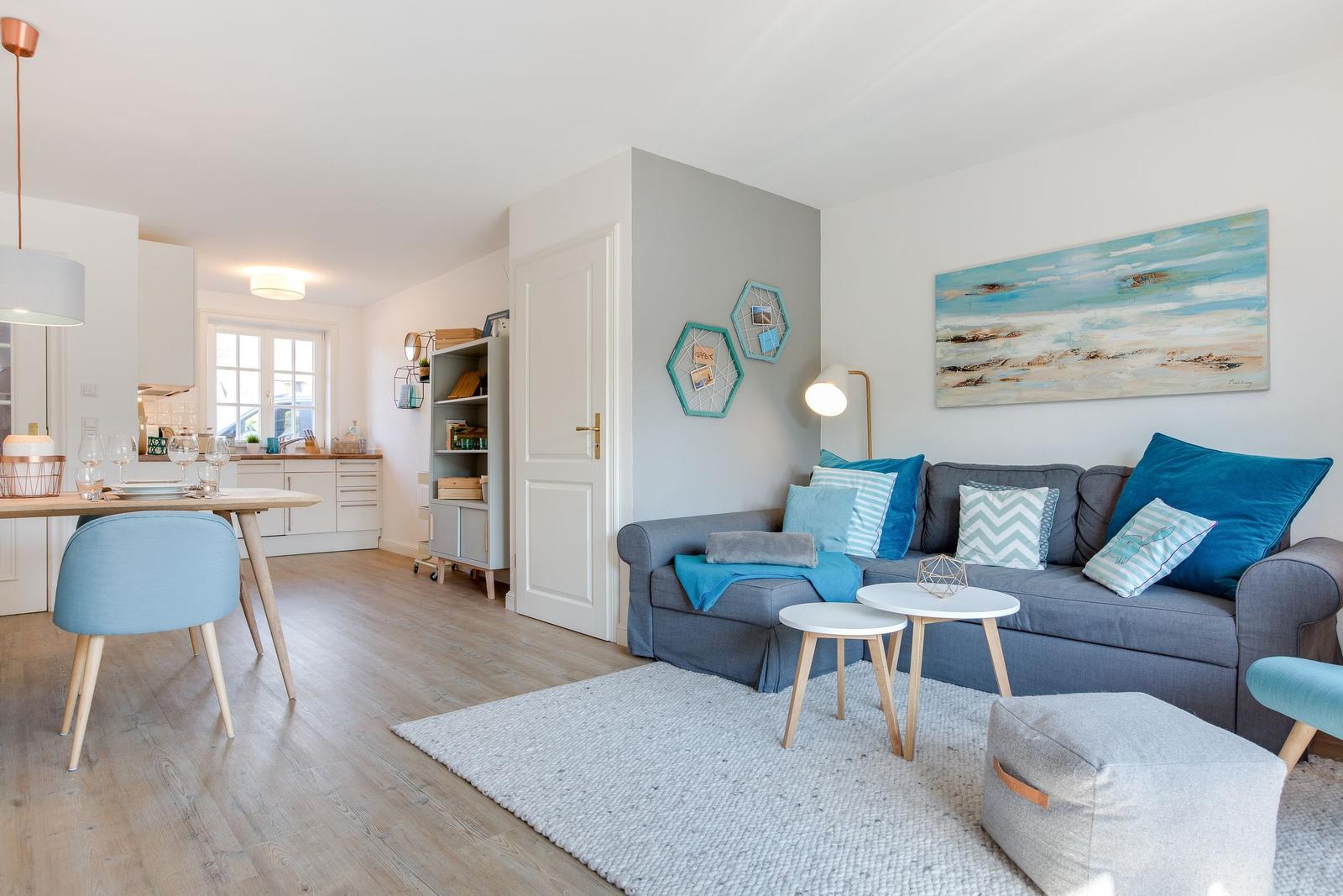 Wohnbereich mit Sofa, Tischen und Küchenbereich im Hintergrund.
