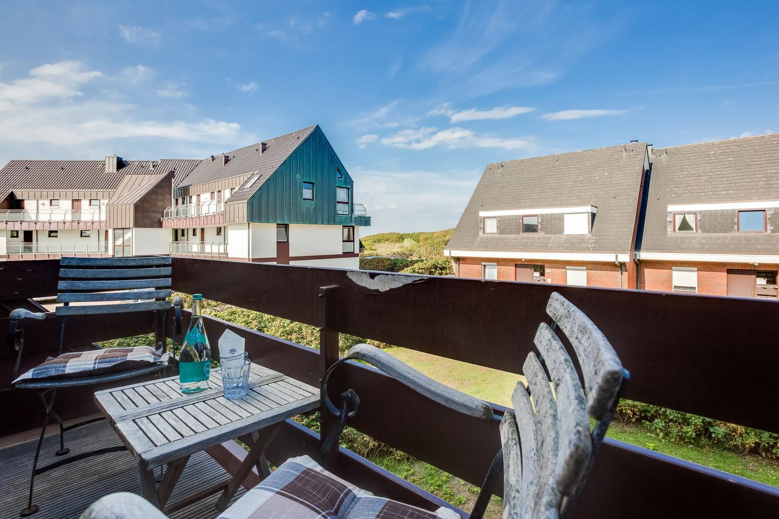 Terrace with table, chairs, and bottle. View of houses and green areas.
