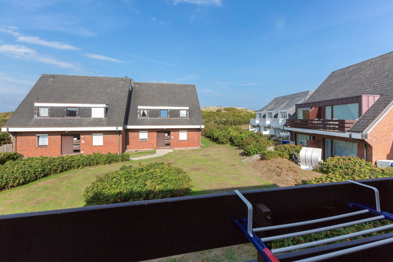 Villa with balcony, green areas, and neighboring houses under blue sky.