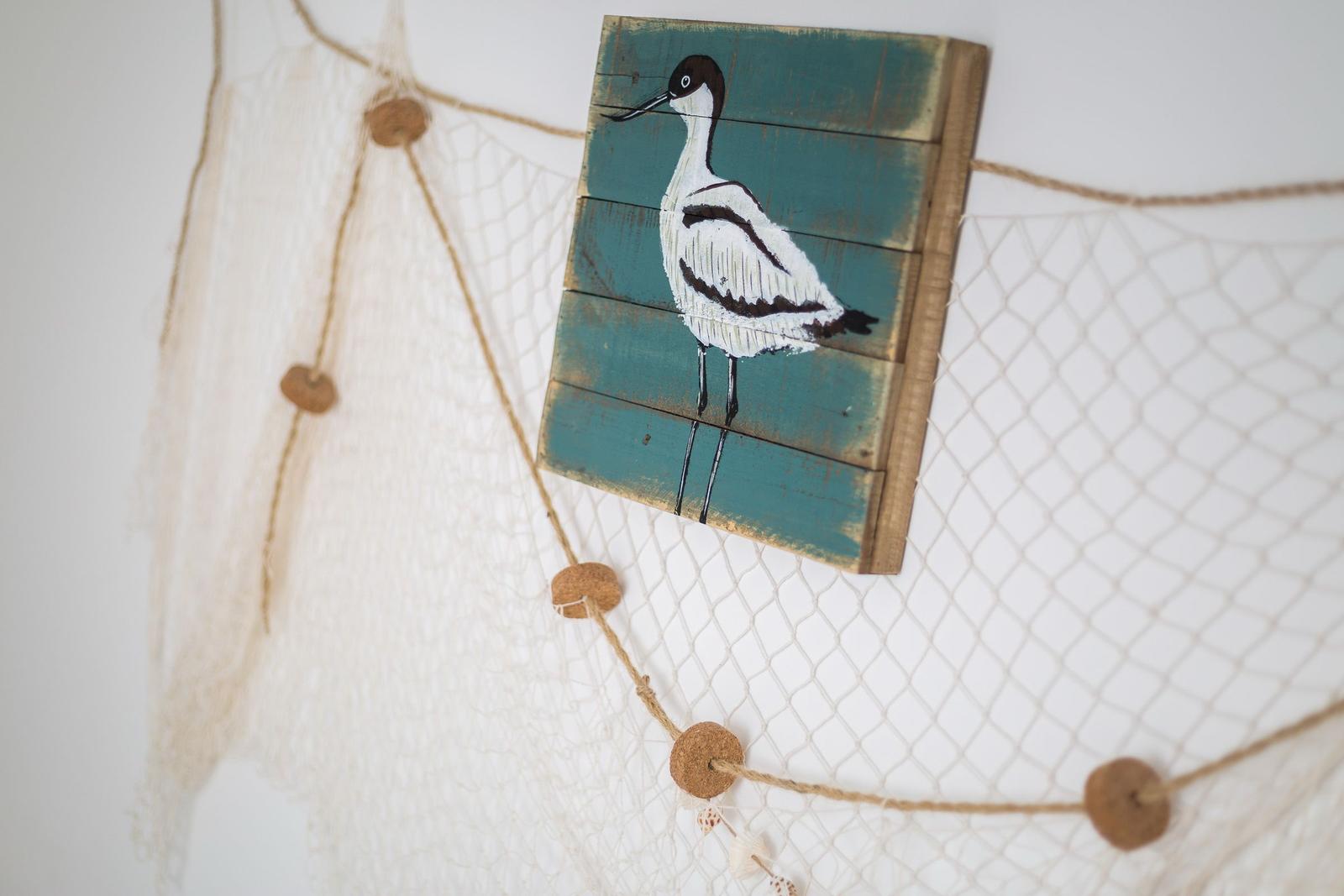 Wooden panel with bird motif hangs on fishing net with wooden beads.