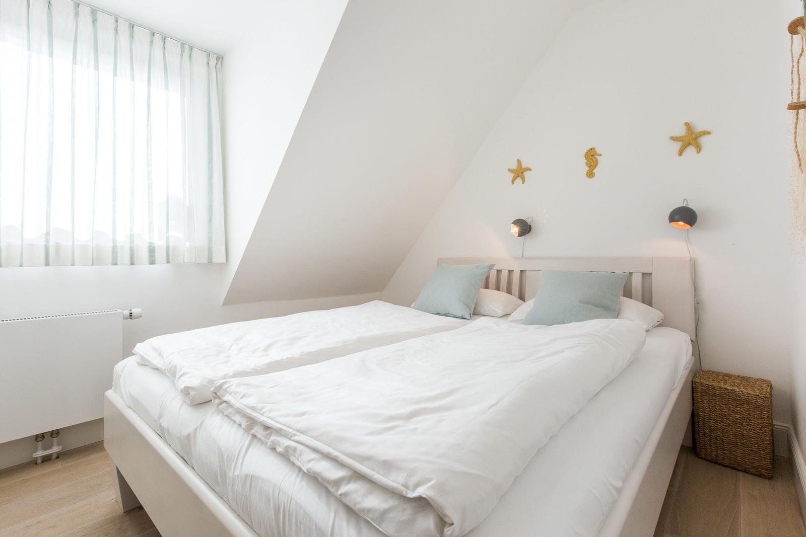 Bedroom with sloped ceiling, bed, window, and wall decor.