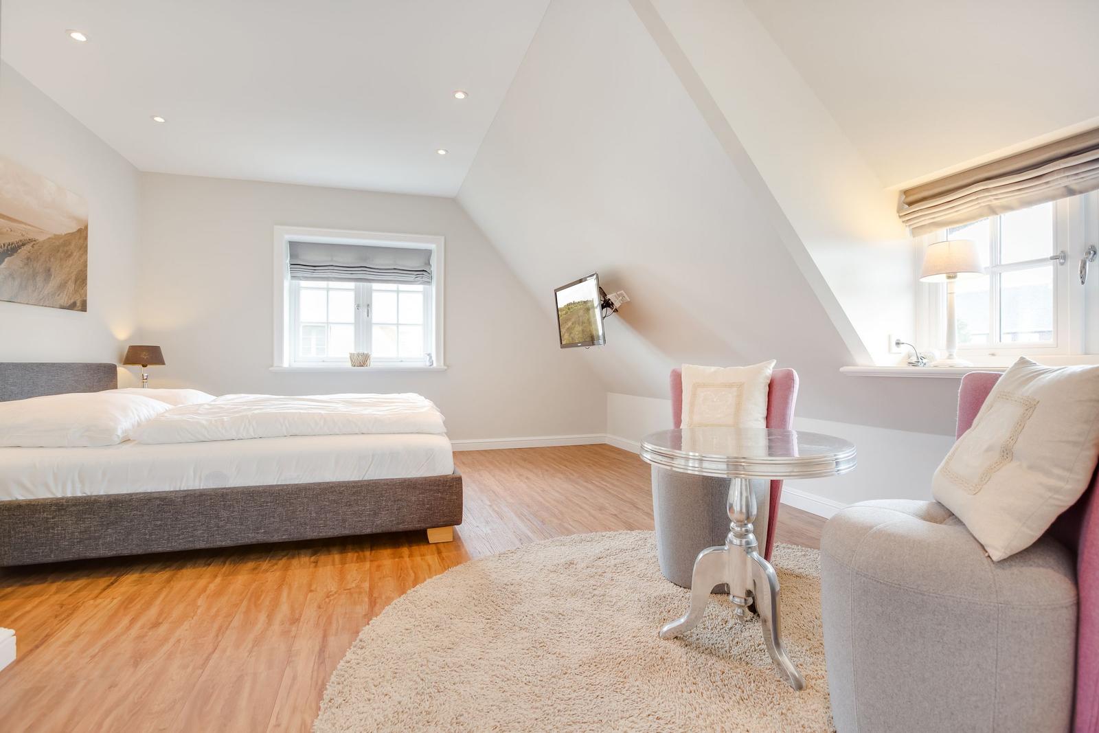 Schlafzimmer mit Dachschräge, Bett, Sessel und TV.