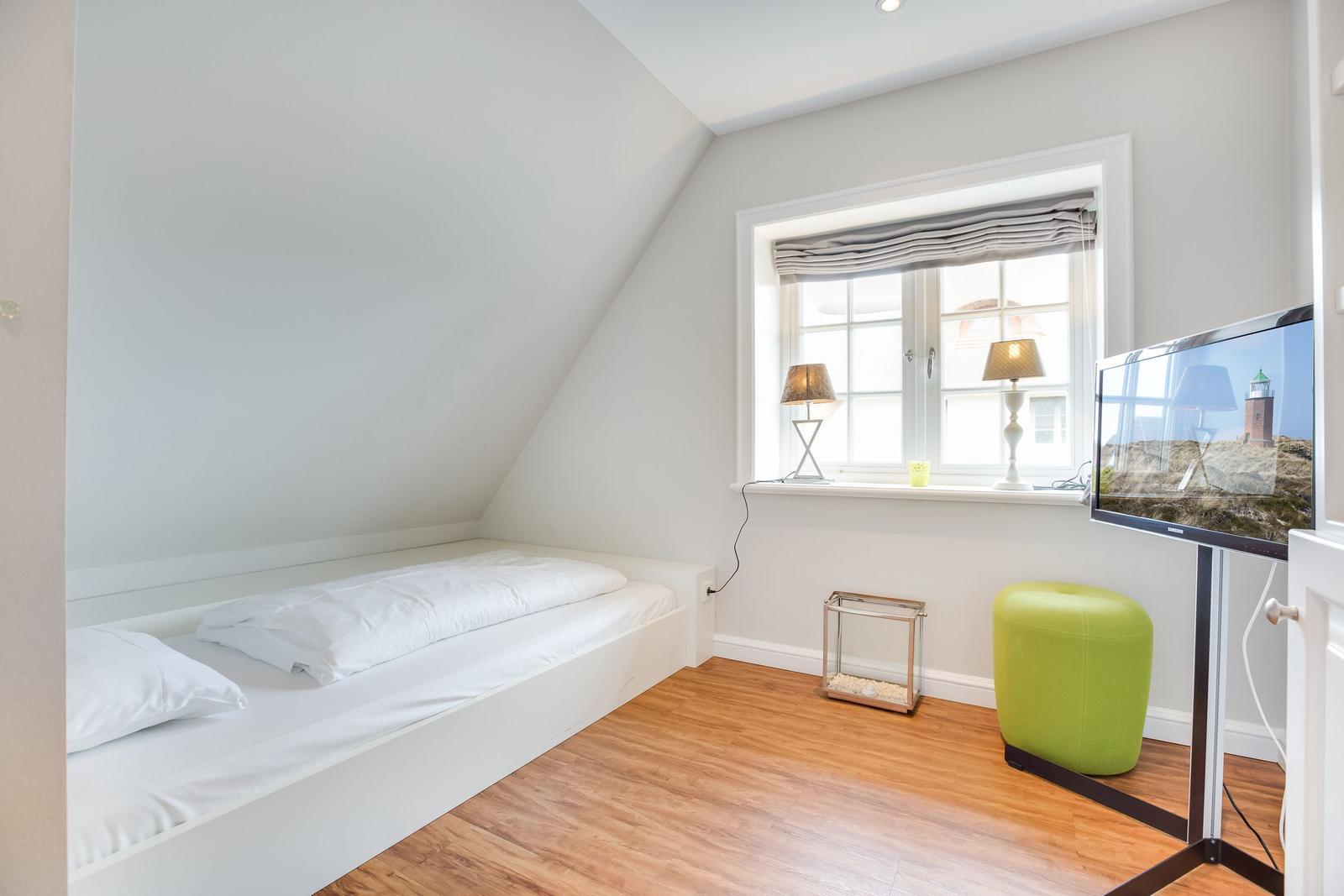Schlafzimmer mit Bett, Fenster und Fernseher auf Ständer.