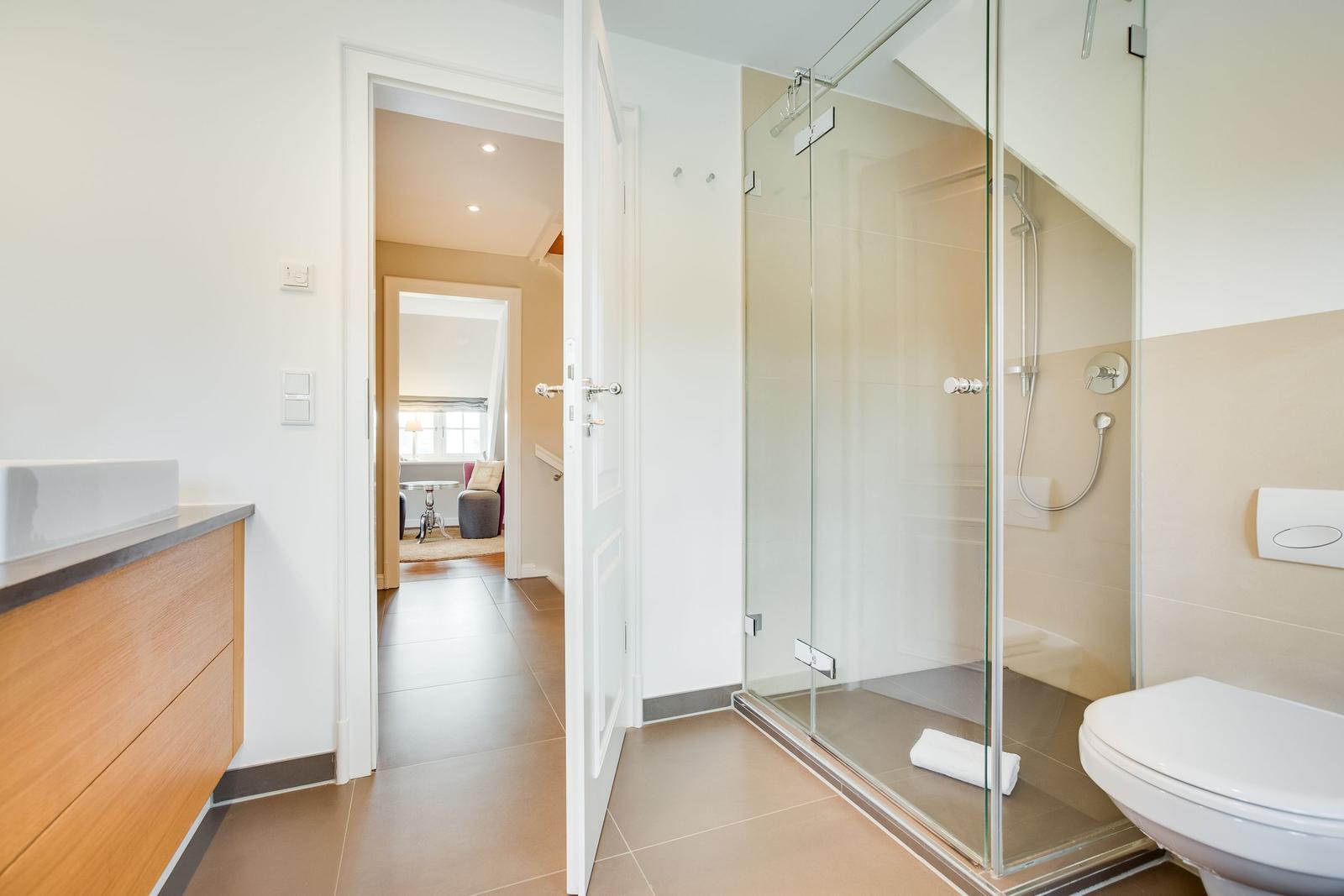 Badezimmer mit Dusche, Toilette und Waschbecken. Durchgang zur Wohnfläche.