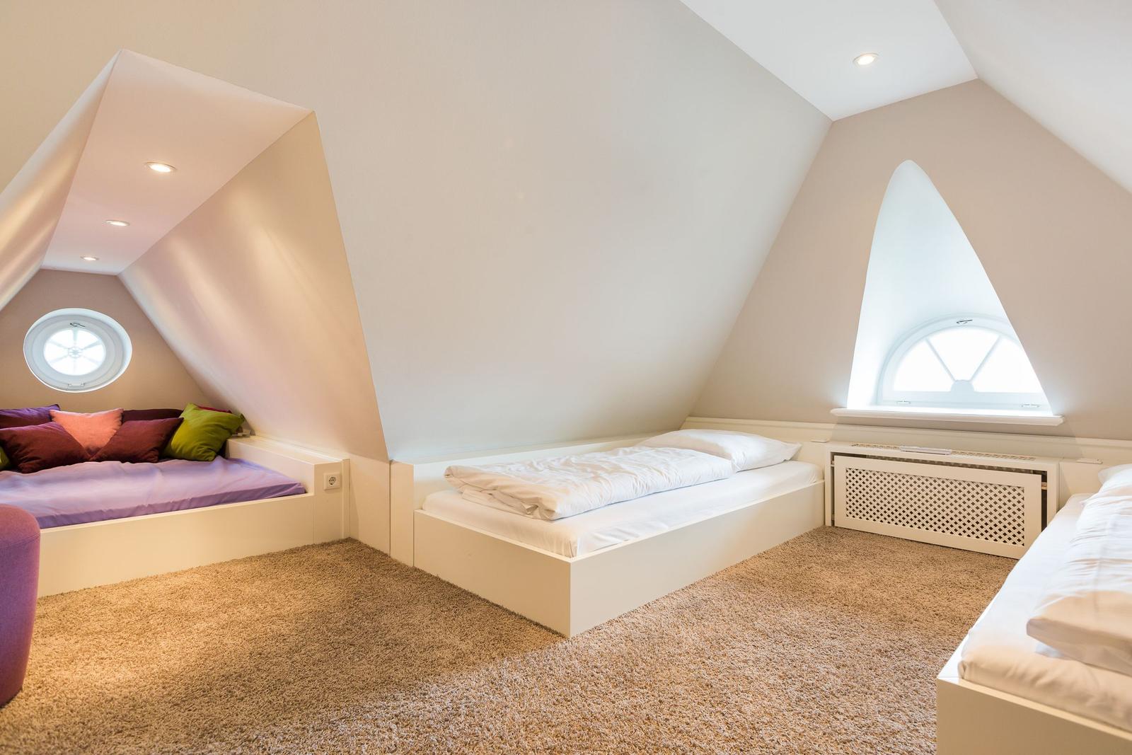 Dachgeschosszimmer mit drei Betten und zwei Fenstern.
