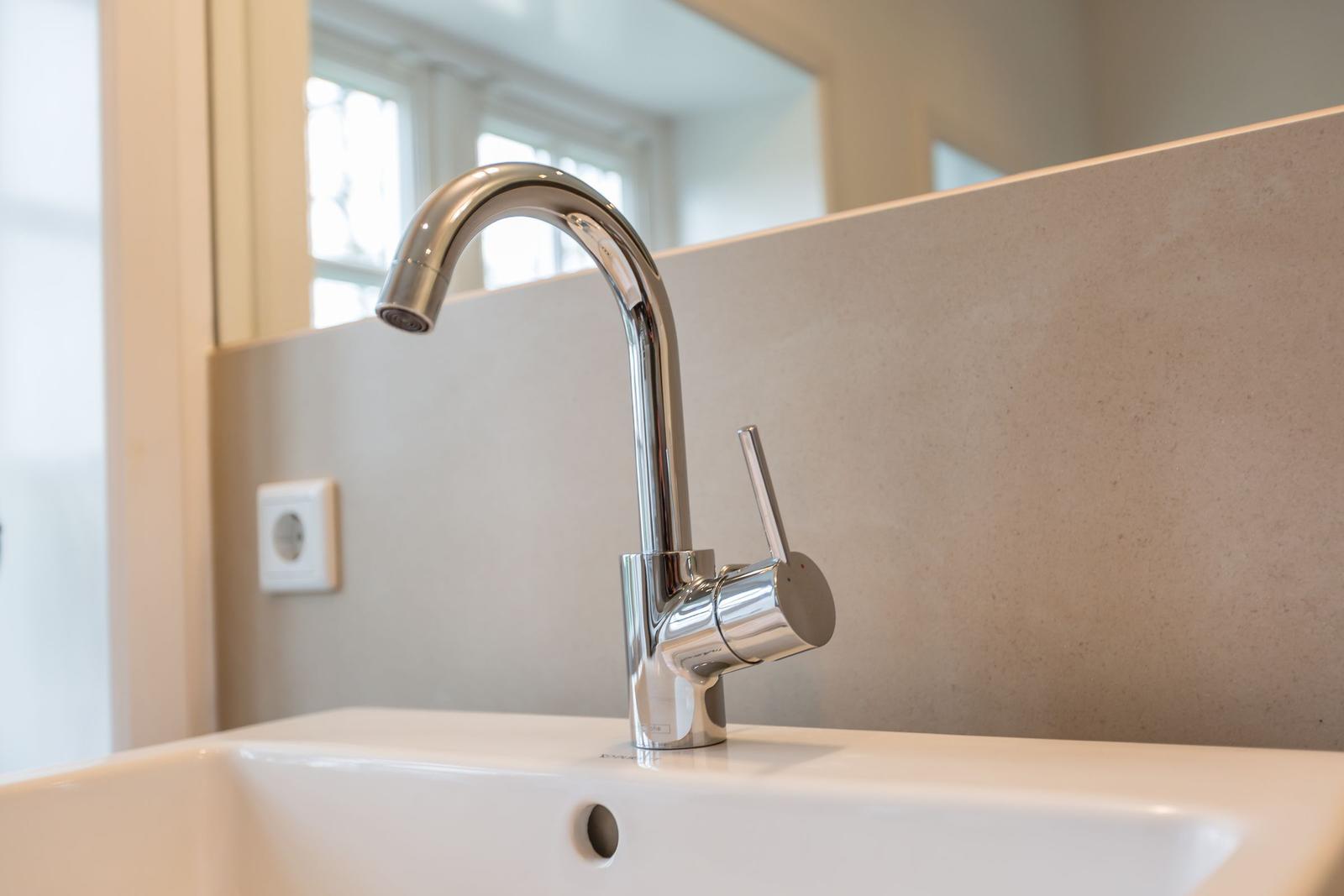 Moderne Waschbecken mit chromfarbenem Wasserhahn und Spiegelfläche im Hintergrund.