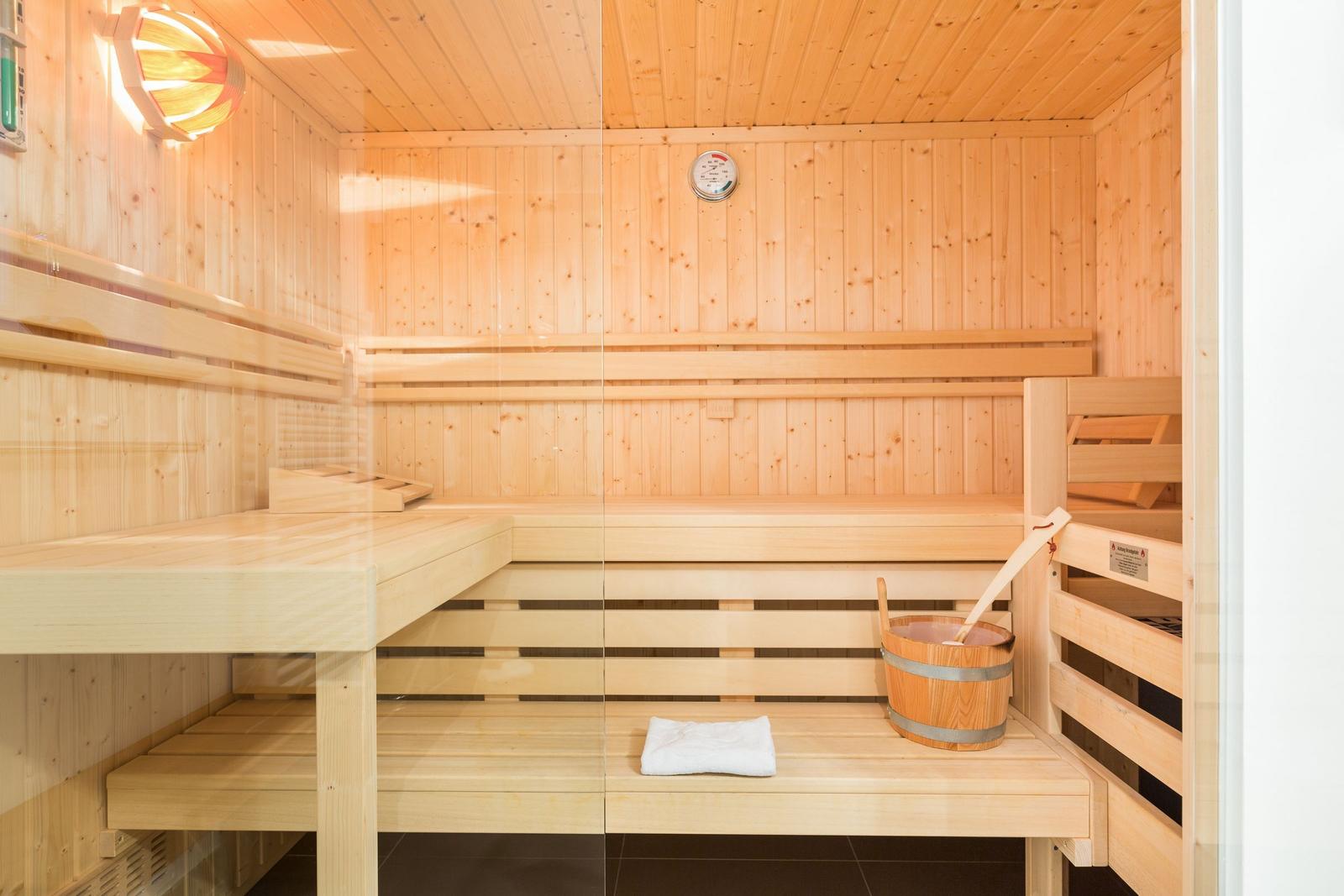 Sauna mit Holzbänken, Thermometer und Eimer mit Löffel.