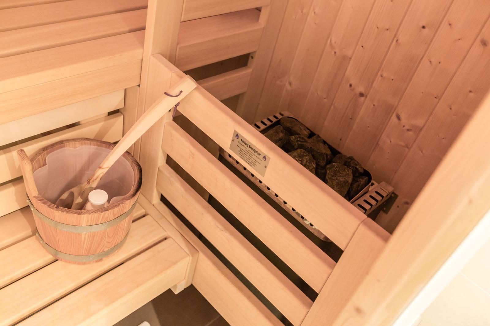 Sauna mit Holzbank, Steinboden und Eimer mit Holzlöffel.