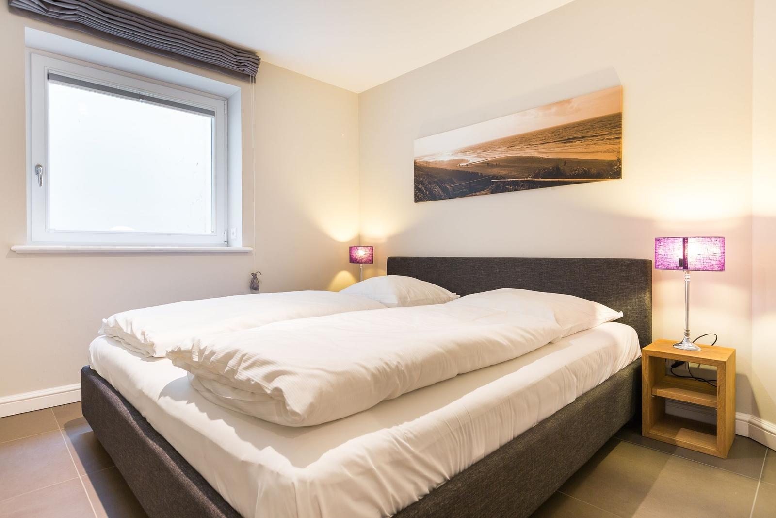 Schlafzimmer mit Doppelbett, Fenster und Nachttisch mit Lampe.