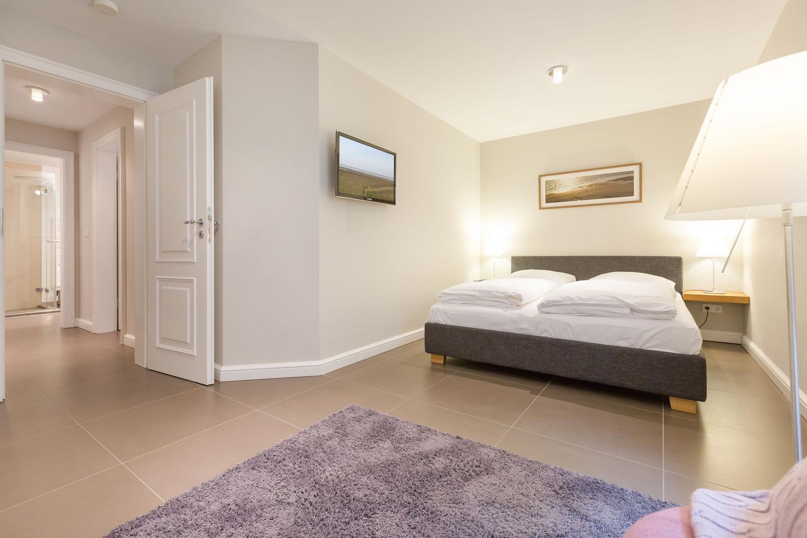 Schlafzimmer mit Bett, Fernseher und Tür zum Bad.