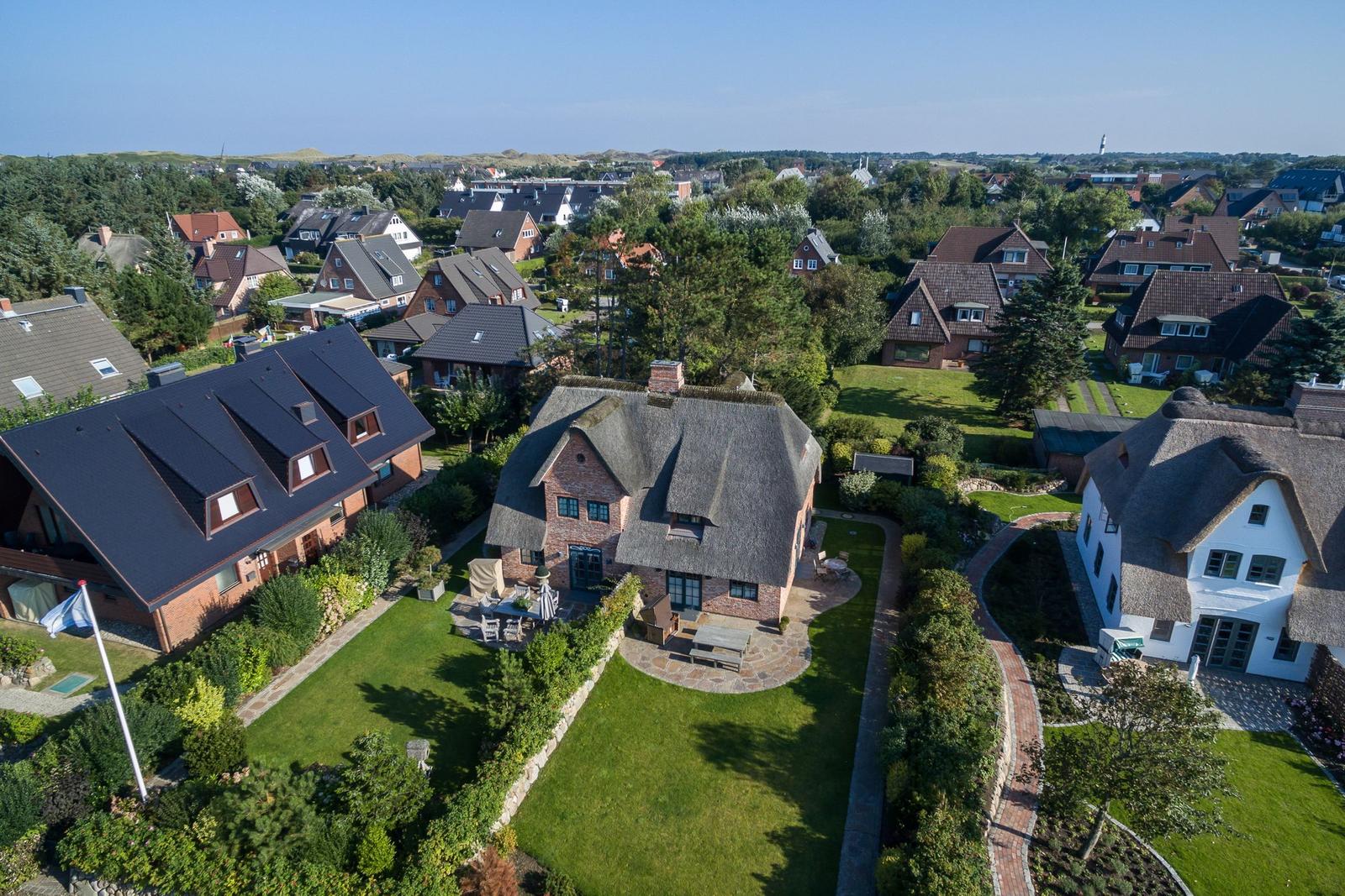 Haus mit Strohdach und Garten, umgeben von weiteren Häusern und Grünflächen.
