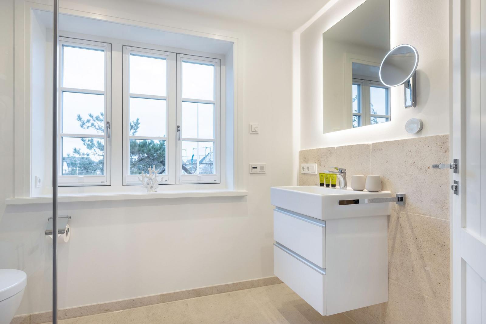 Badezimmer mit Dusche, Waschbecken und Fenster mit Blick auf Bäume.