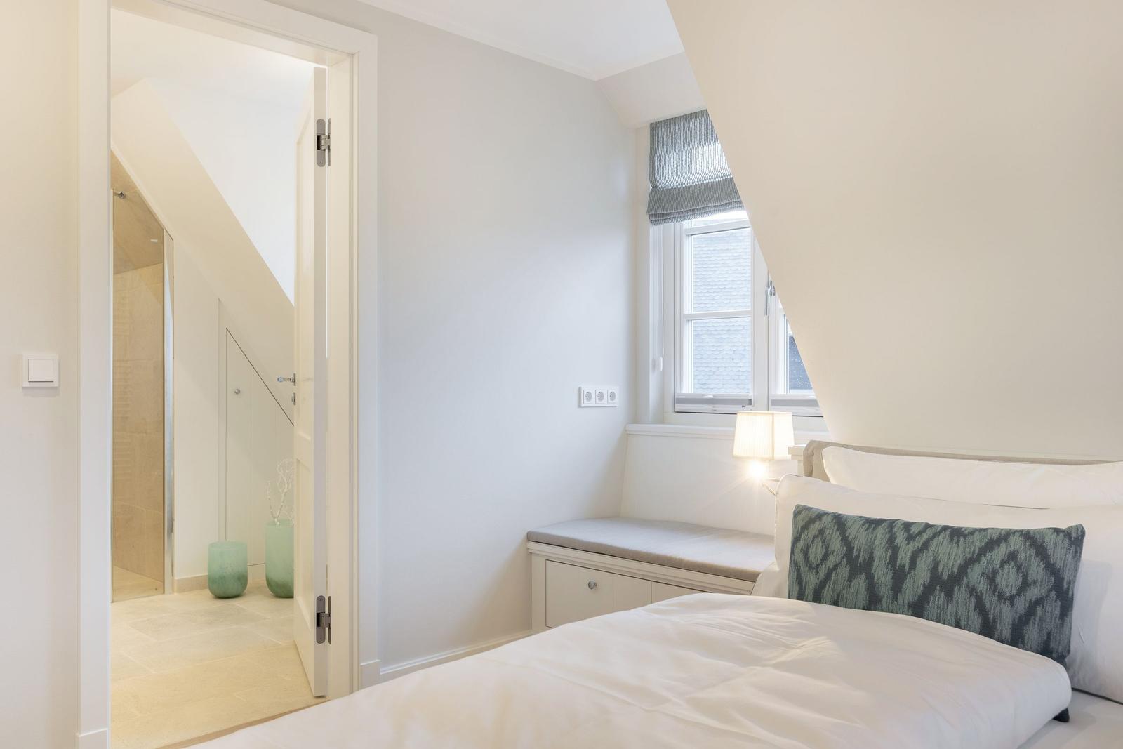 Schlafzimmer mit Bett, Fenster und Blick in Badezimmer