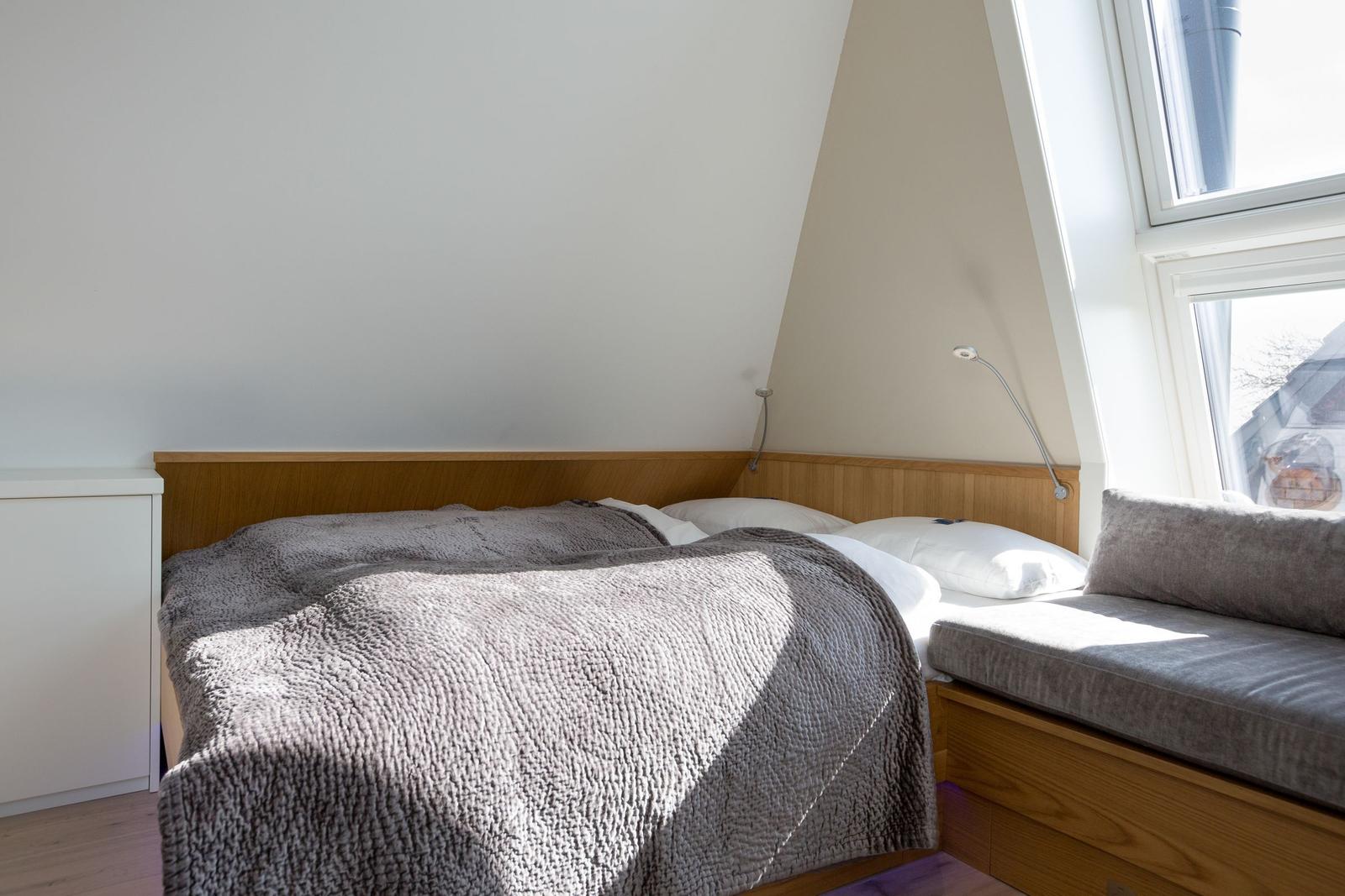 Schlafzimmer mit Dachschrägen, Bett, Fenster und Nachttisch.