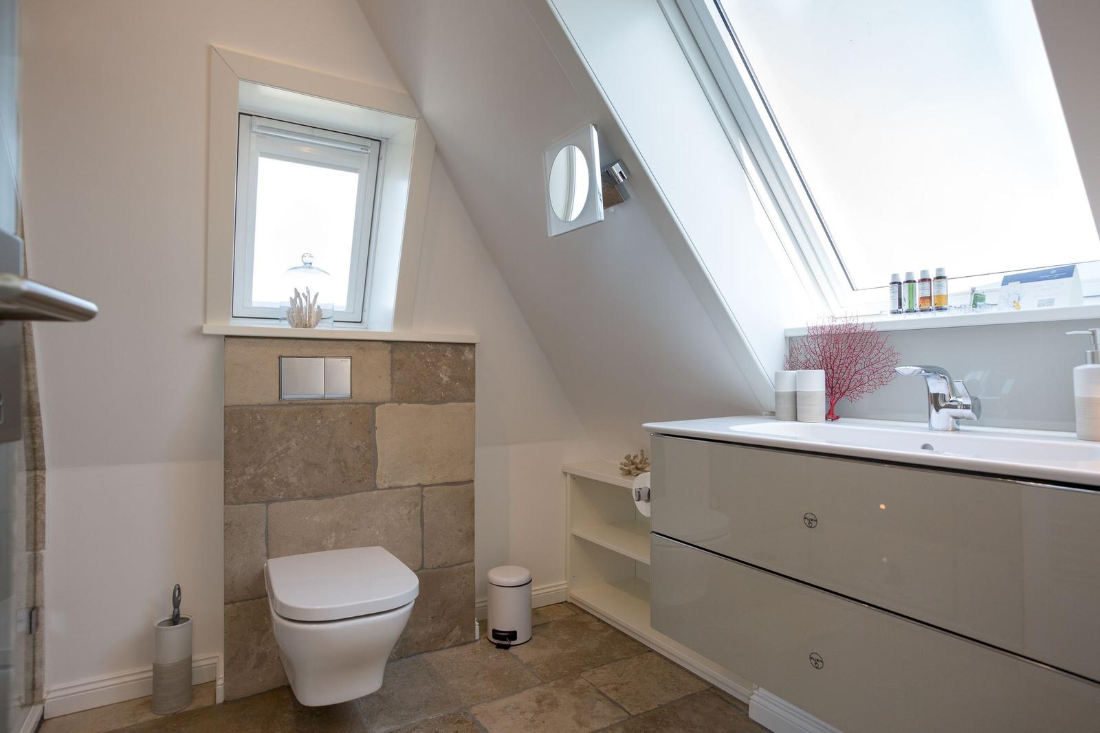 Badezimmer mit Dachschrägen, Waschbecken und Toilette unter Fenster