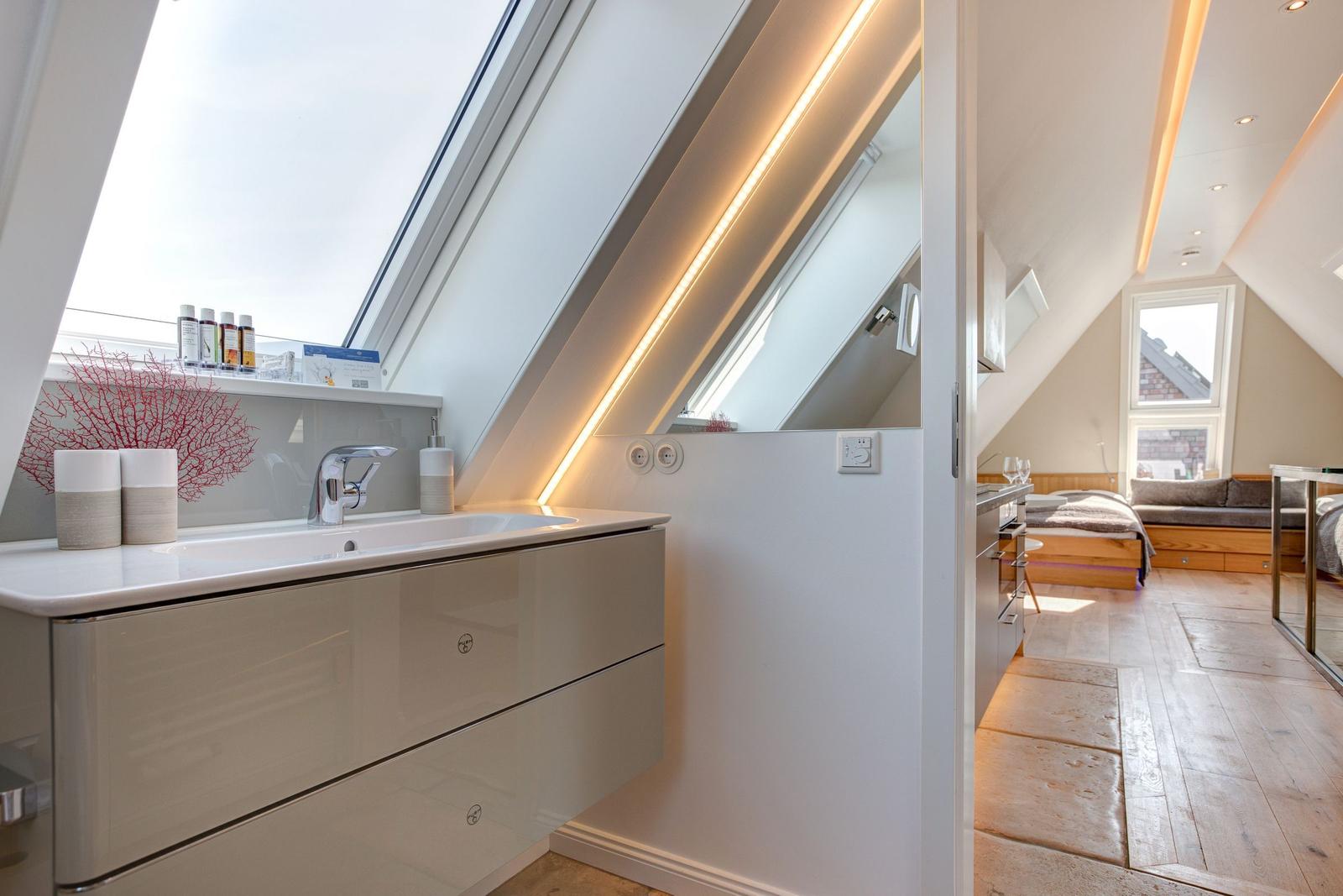 Duschbad mit Dachfenster und Spiegelschrank. Blick in Schlafzimmer mit Holzboden.