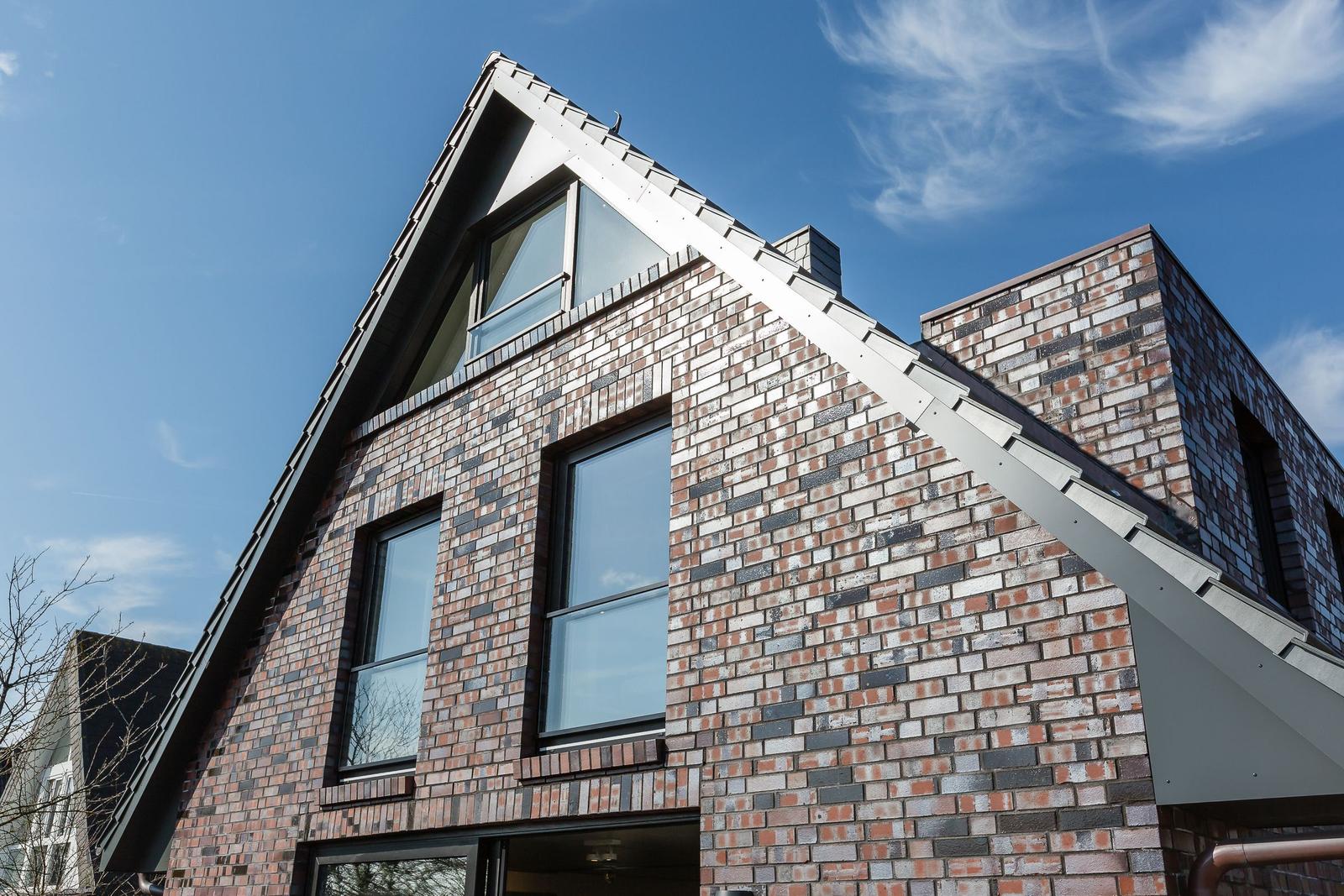 Modernes Haus mit Ziegelfassade und großen Fenstern unter blauem Himmel.