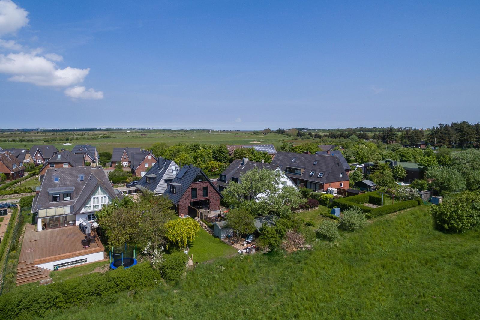 Überblick über Wohnhäuser mit Gärten und Grünflächen unter blauem Himmel.