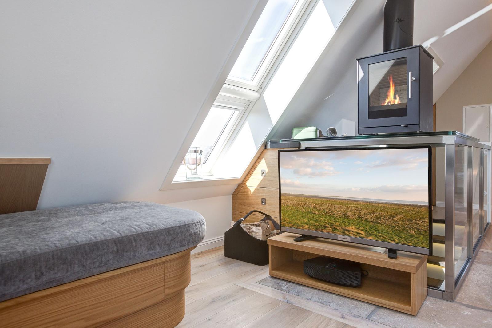 Dachgeschosszimmer mit TV, Kamin und Dachfenstern.