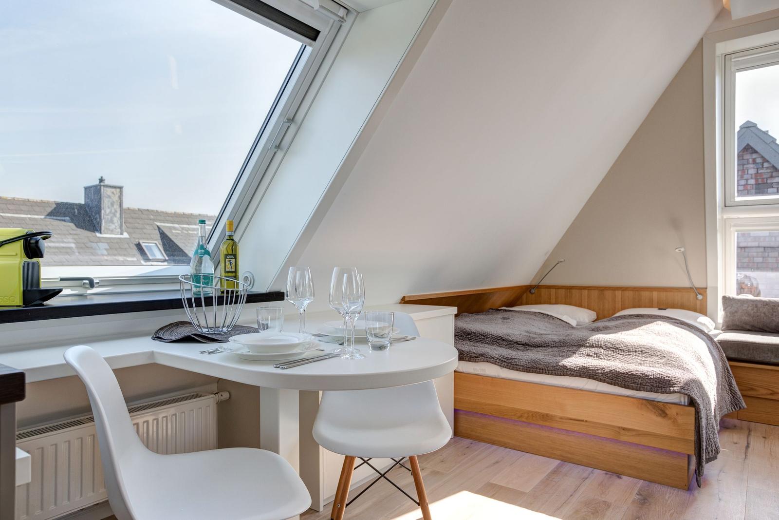Schlafzimmer mit Dachfenster, Esstisch und Bett unter Dachschräge.