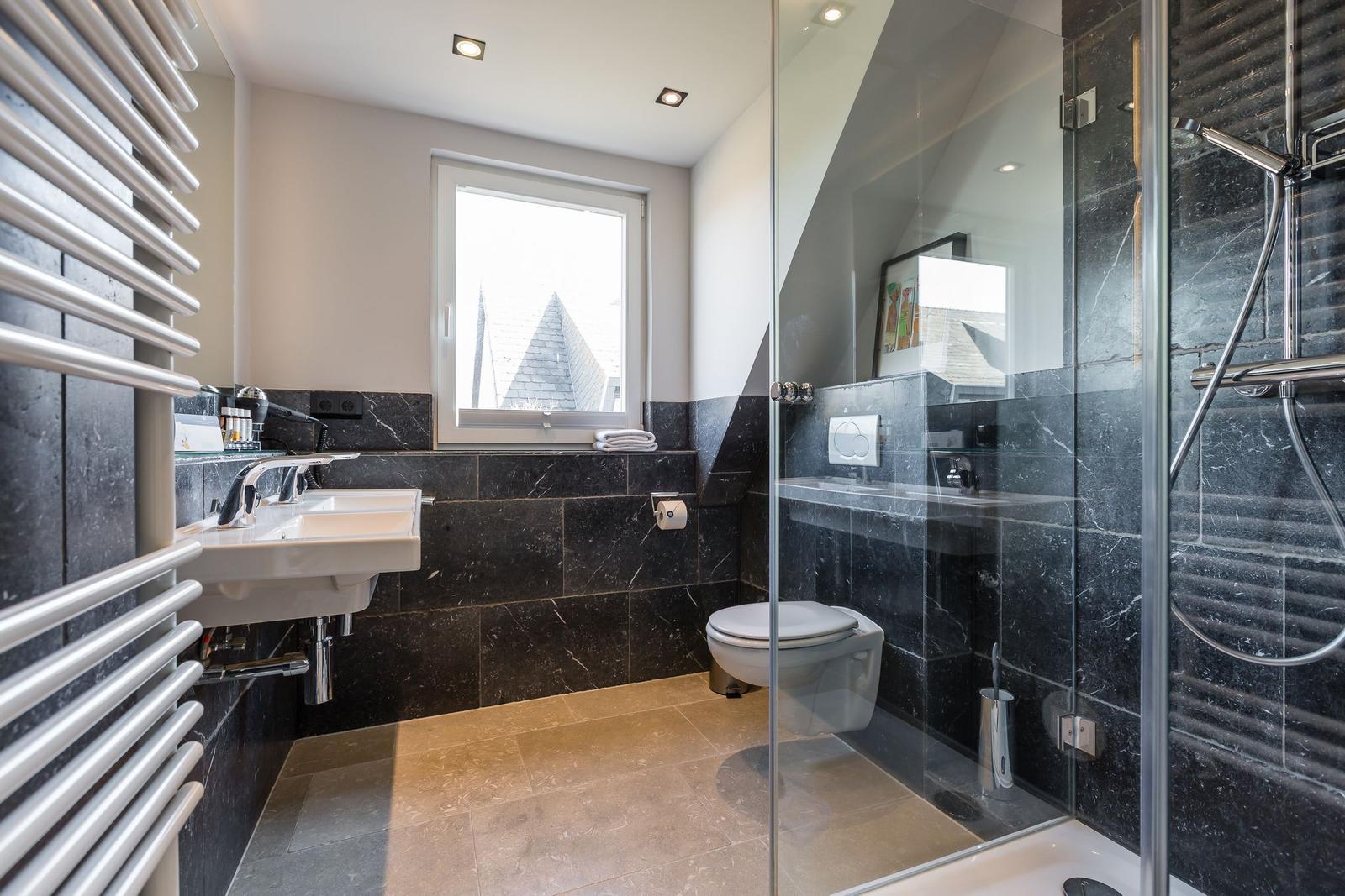 Bathroom with shower, toilet, and sink. Black marble wall and window with view.