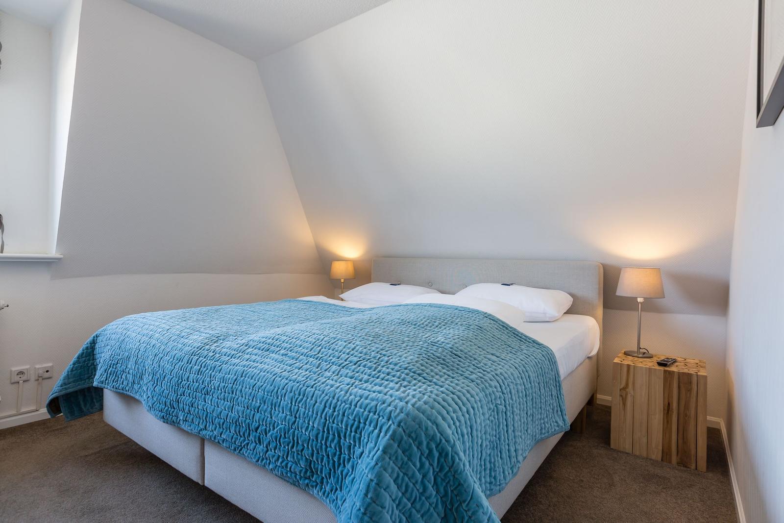 Bedroom with sloped ceiling, bed with blue quilt, and two nightstands.