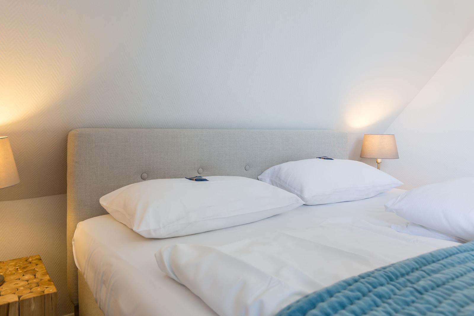 Double bed with white pillows and bedding. Wooden nightstand and lamp.