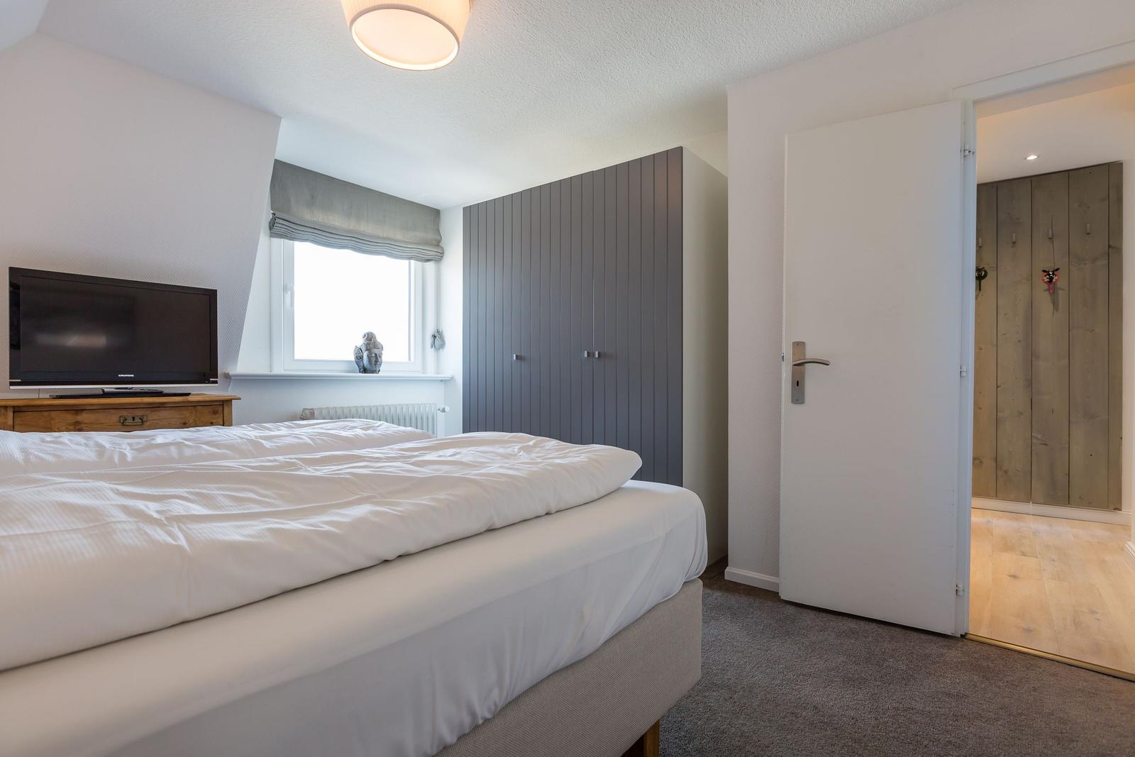 Bedroom with bed, TV, and wardrobe. Door leads to adjacent room.