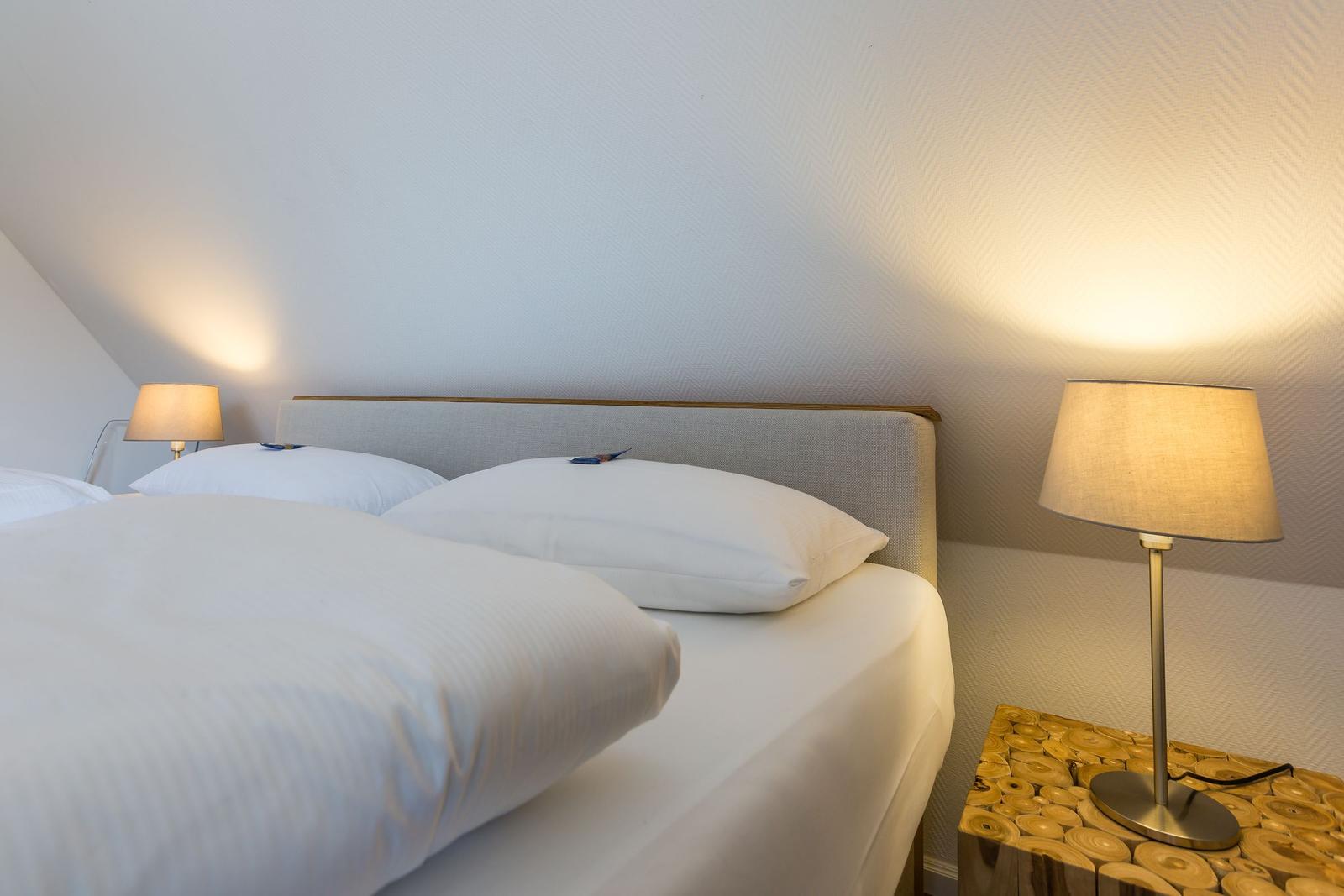 Double bed with white pillows and bedding under slanted walls with nightstands and lamps.