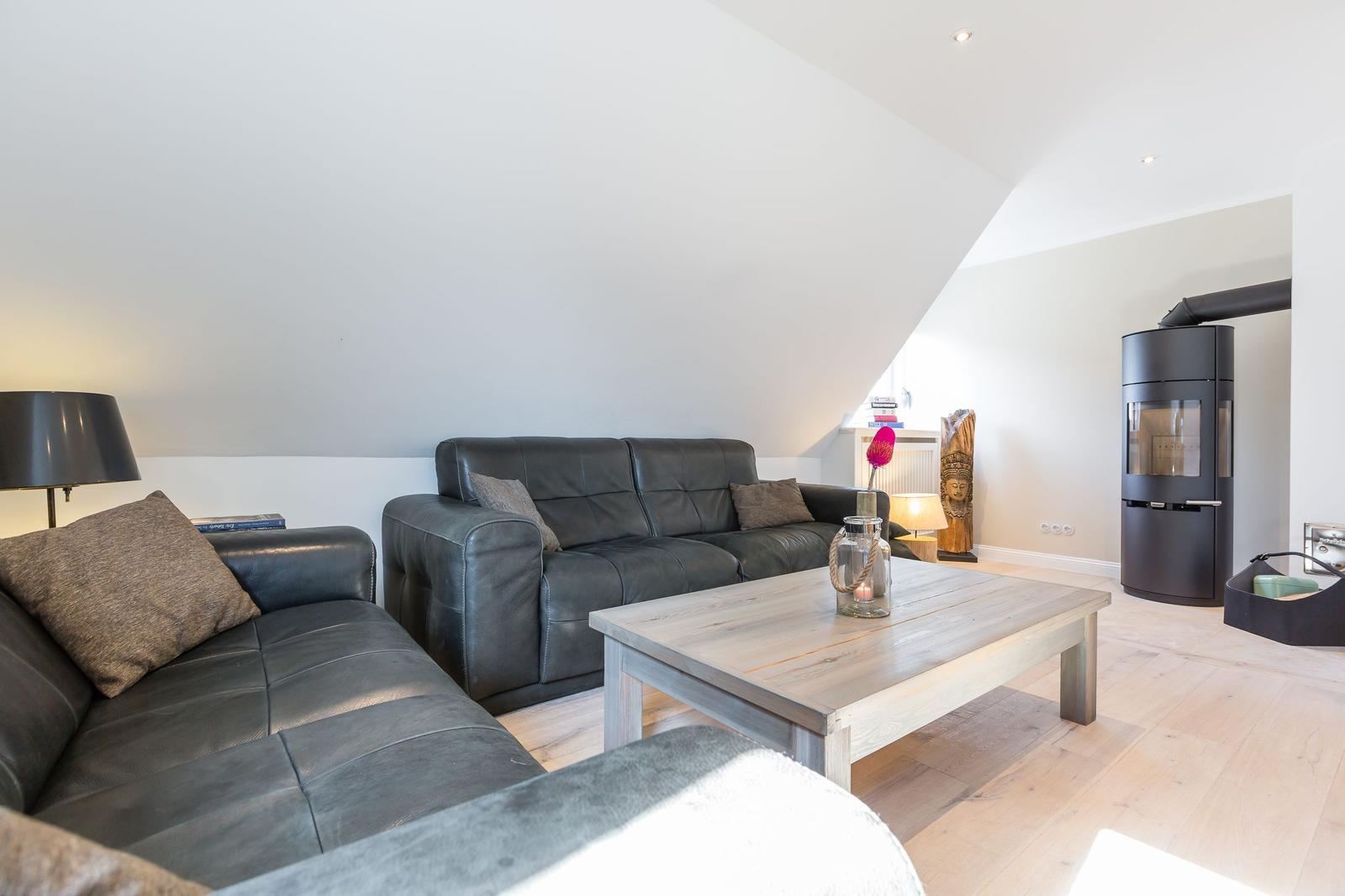 Living room with leather sofa, wooden table, and wood stove under sloped ceiling.