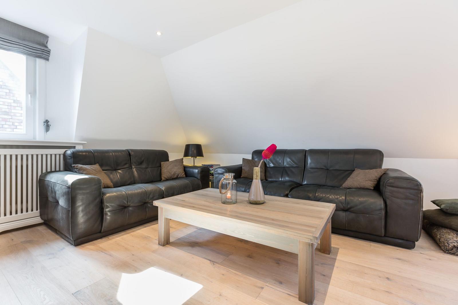 Two dark leather sofas surround a wooden table. Wooden floor and white walls.