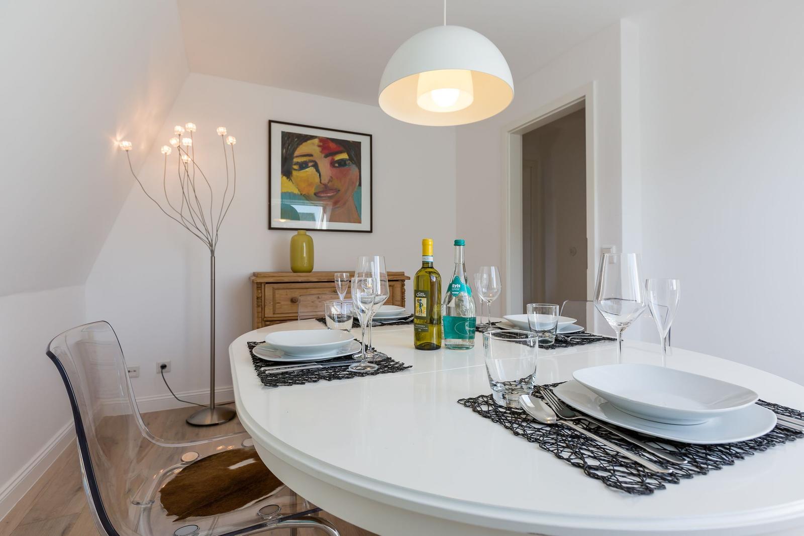 Round table with dishes and bottles. Transparent chairs and wall art.