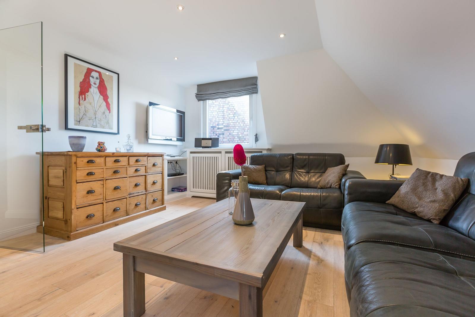 Living room with leather sofa, wooden table, and cabinet. Window with roller blind. Sloped ceiling.