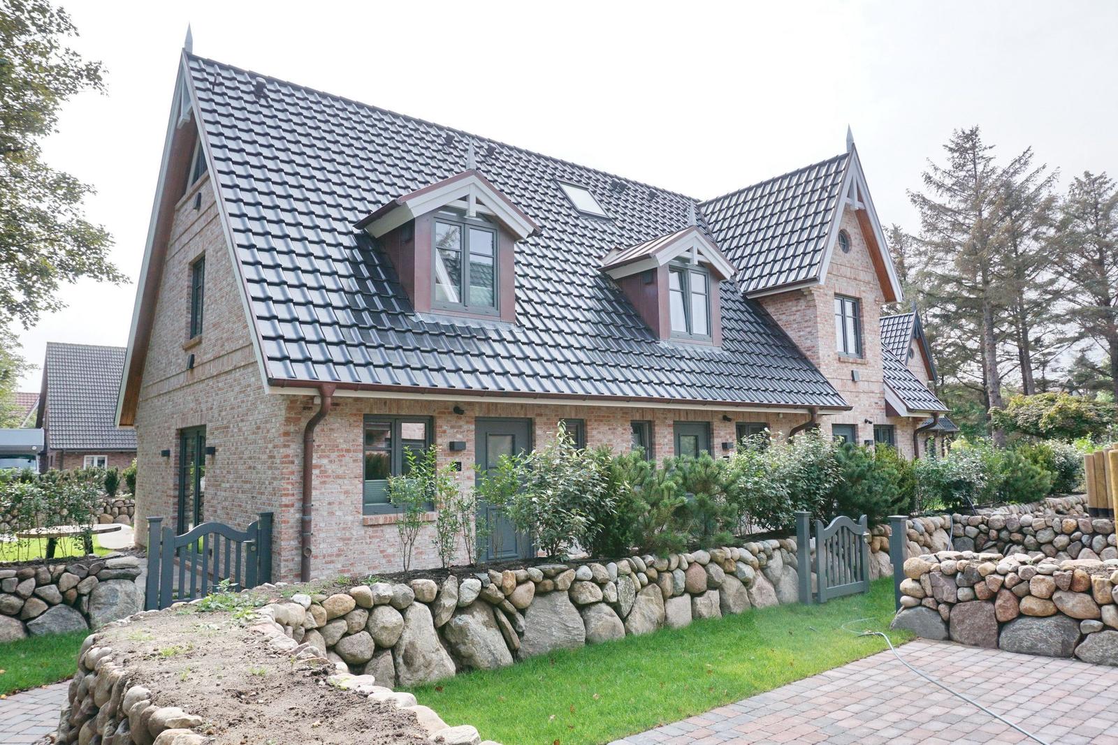 House with stone wall, green lawn, and dark roof