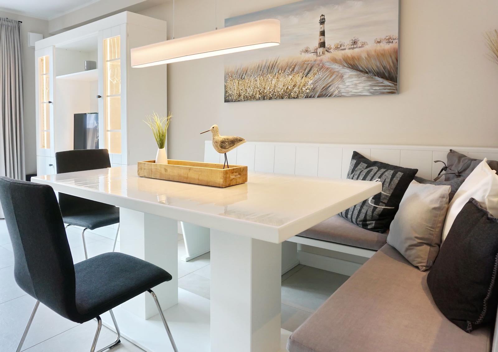 Dining area with white table, bench, and wall art with lamp.