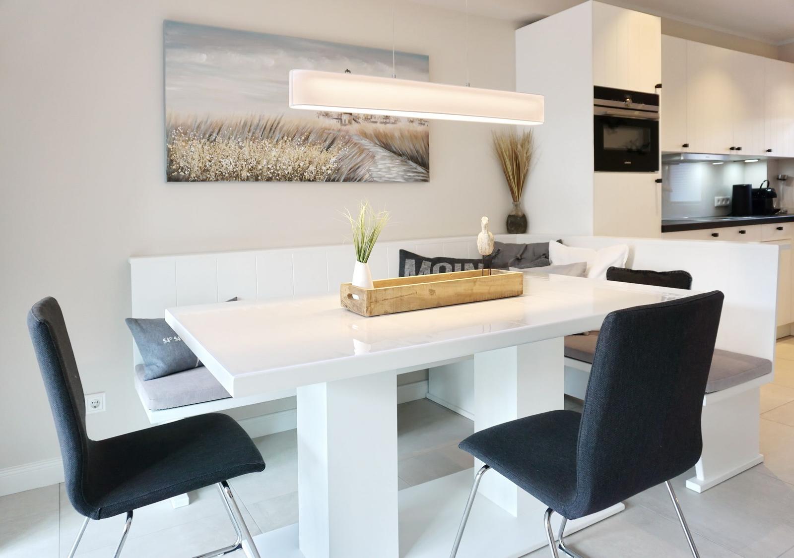 Dining area with white table, dark chairs, and bench. Wall art and ceiling light.