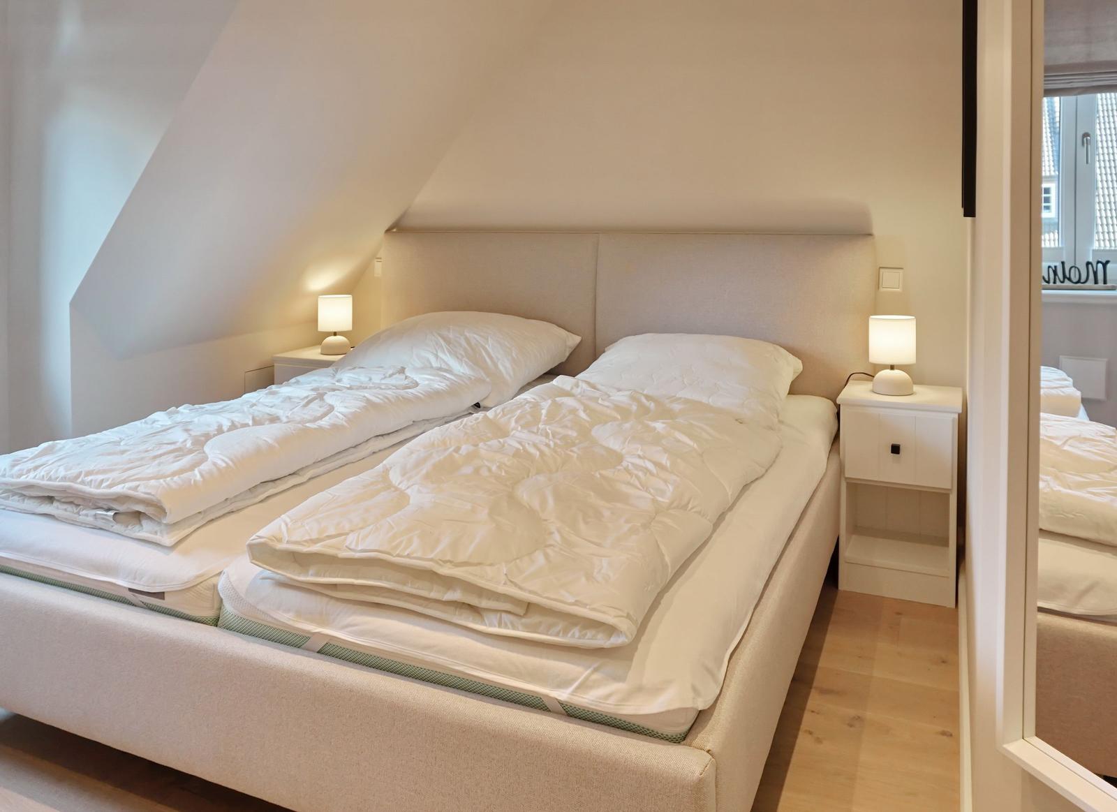 Bedroom with double bed, nightstands, and lamps under sloped ceiling.