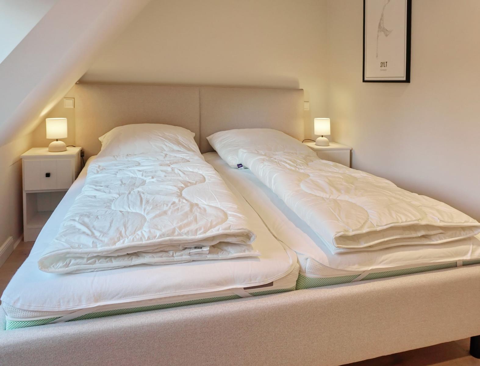 Double bed with two mattresses and white bedding under sloped ceiling