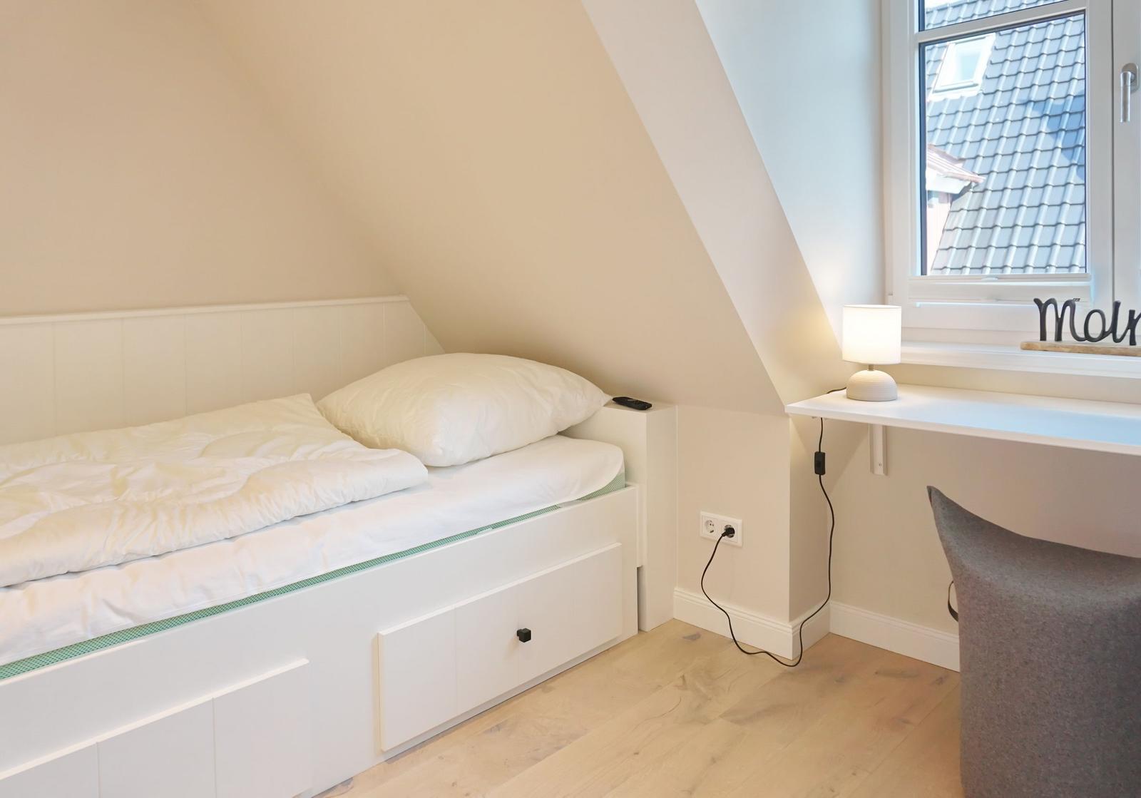 Bedroom with sloped ceiling, bed, desk, and window.