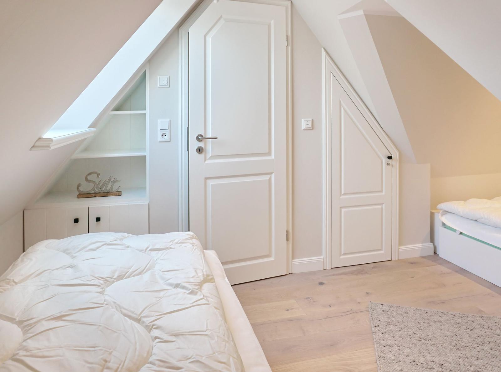 Bedroom with sloped ceilings, white door, and bed with white bedding.