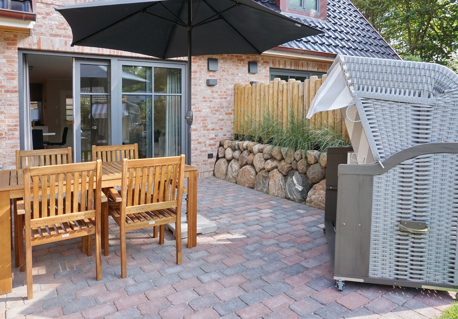 Terrace with wooden table, chairs, and umbrella. Backyard with stone wall and garden.