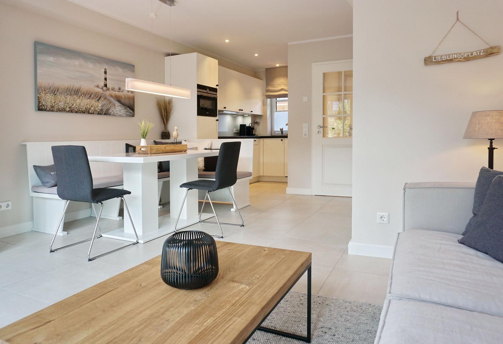 Living and dining area with kitchenette and sofa. Wooden table, gray seating, and wall art.