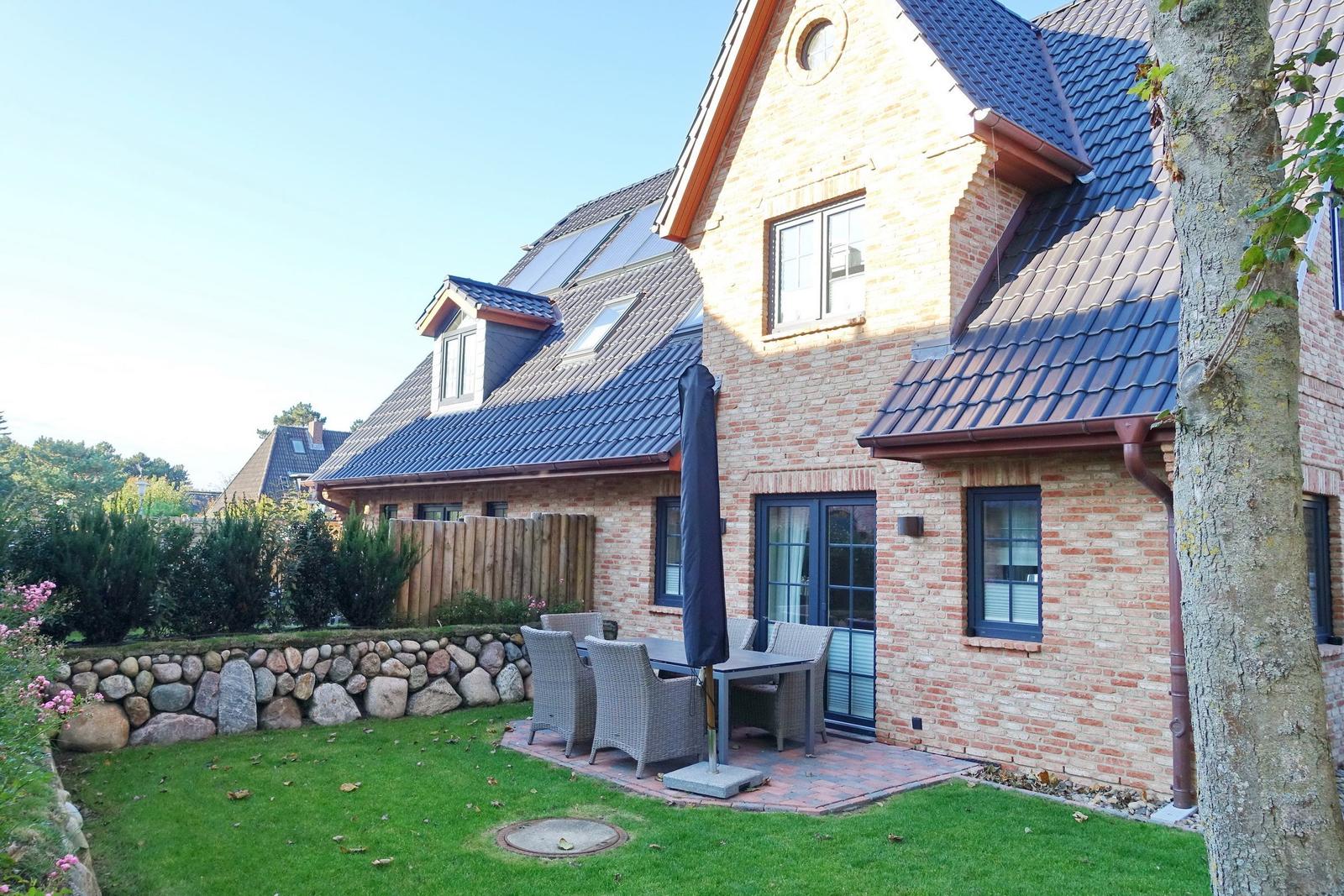 House with terrace, garden, and umbrella. Wooden fence and stone wall surround the garden.