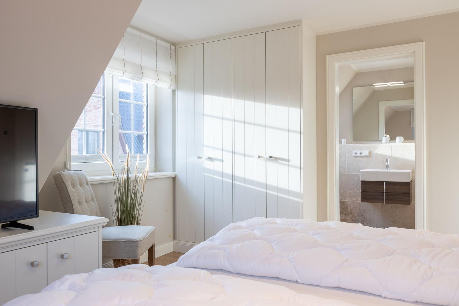 Bedroom with bed, wardrobe, and bathroom. Window with blind and TV.
