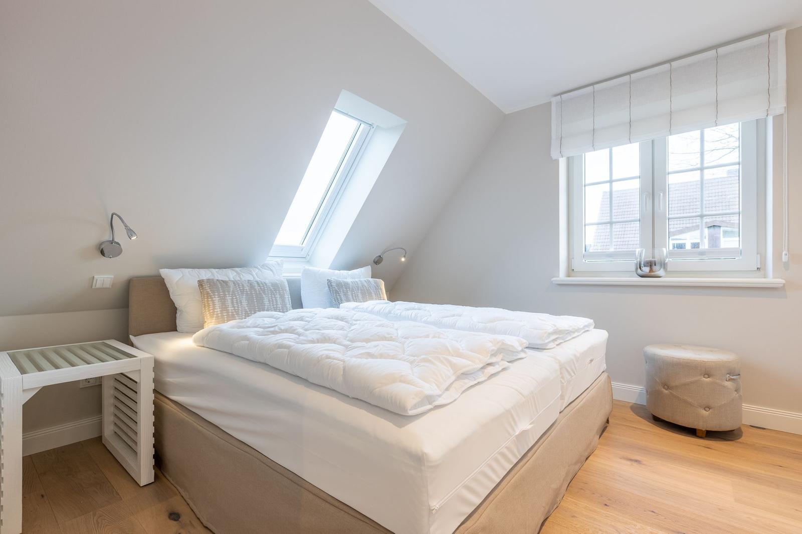 Bedroom with skylight, window and bed with white bedding.