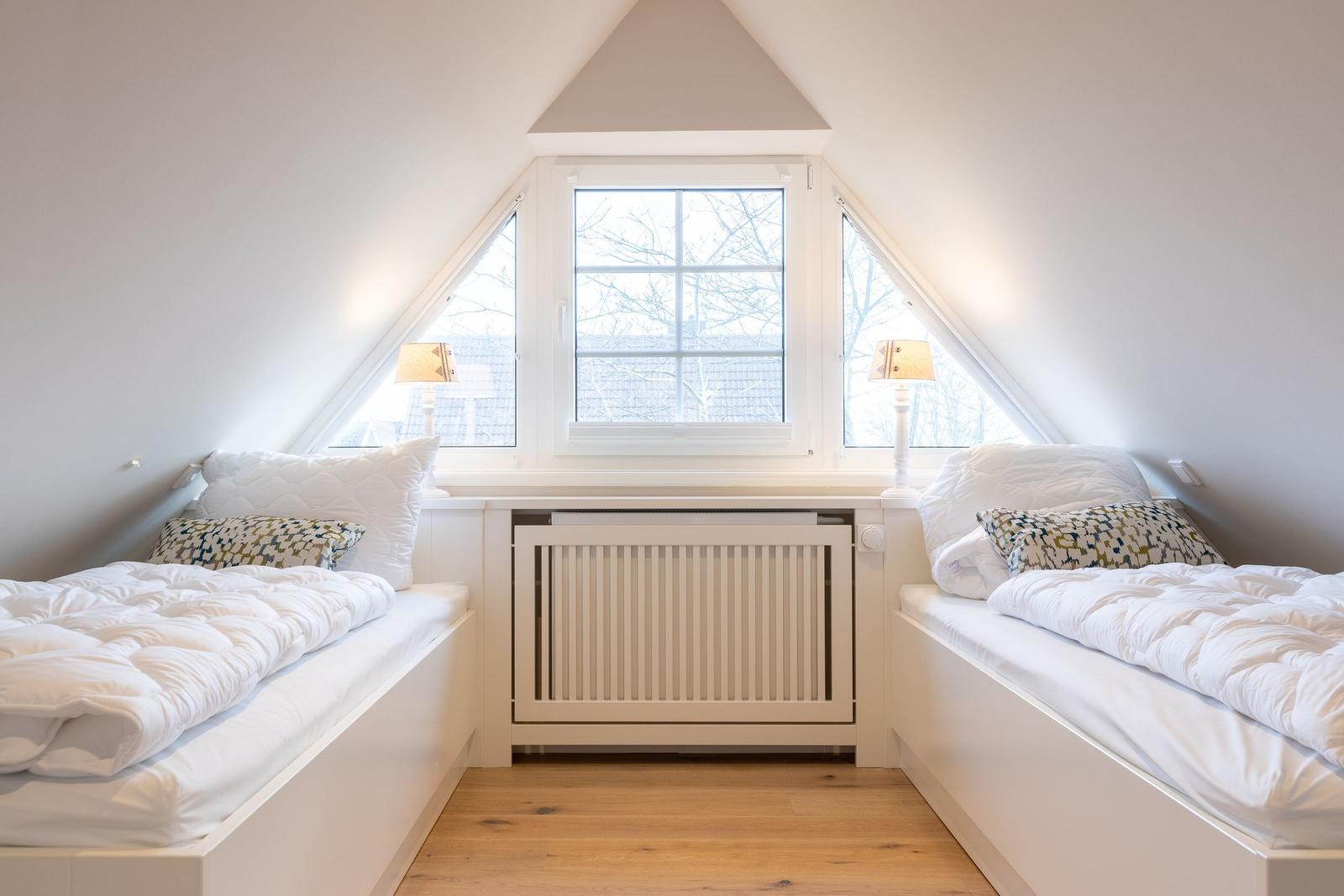 Two beds under a skylight with wooden floor and radiator.