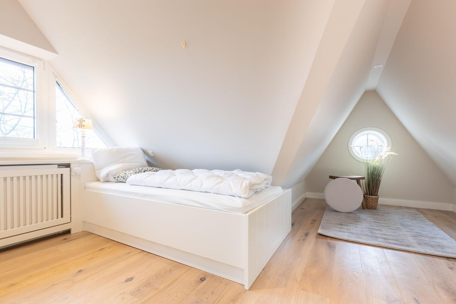 Bedroom with sloped ceiling, window, and bed on pedestal.