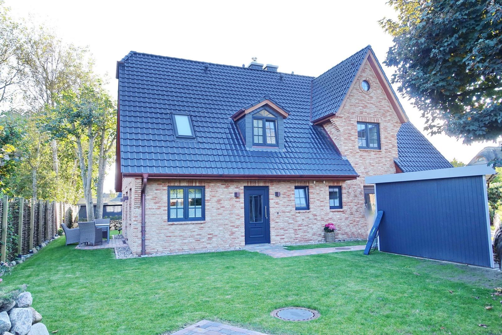 House with brick facade, dark blue roof, and garden with seating area.